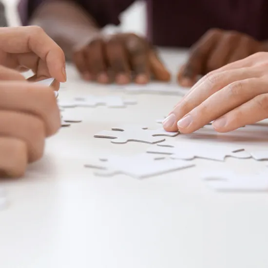 Mehrere Personen sitzen an einem Tisch und fügen Puzzleteile zu einem Ganzen zusammen.