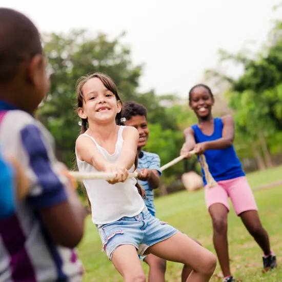 Einige Kinder spielen auf einer Wiese Seilziehen.