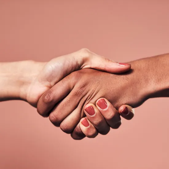 Zwei Hände umfassen sich in einem herzlichen Handschlag vor rosafarbenem Hintergrund – Symbolbild für Unterstützung und Vertrauen.