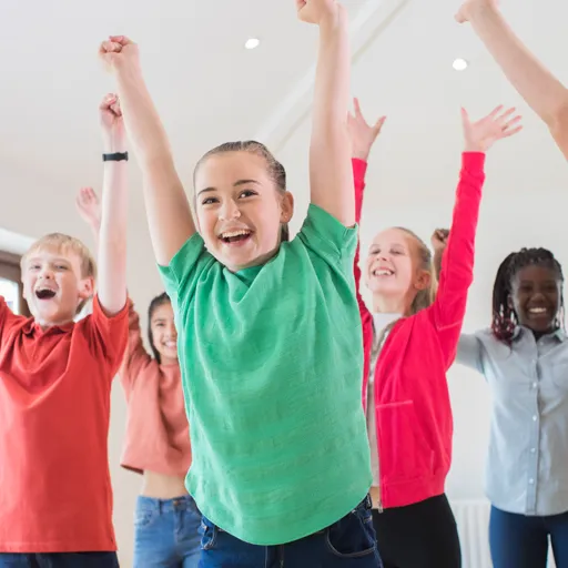 Eine Gruppe von Kindern jubelt mit erhobenen Armen und lachenden Gesichtern in einem hellen Raum.