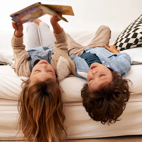 Zwei Kinder liegen auf einem Sofa und stöbern zusammen in einem Buch.